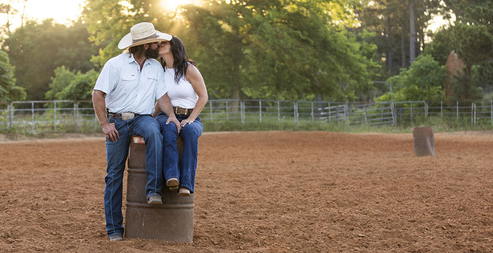 Kip and Kalie Smith sitting on a barrel inside a rodeo arena, kissing.
